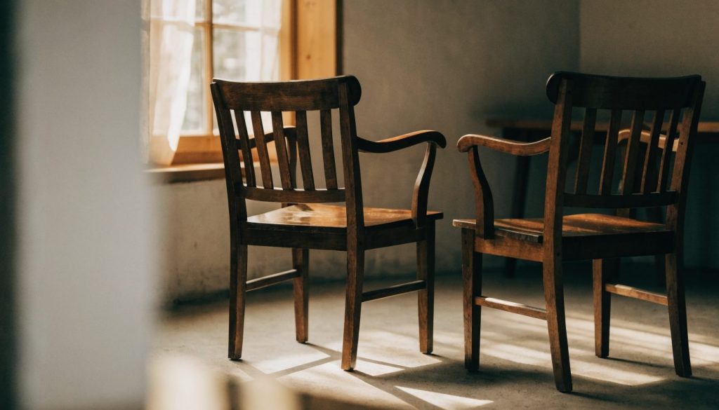 Two empty wooden chairs facing each other in warm window light