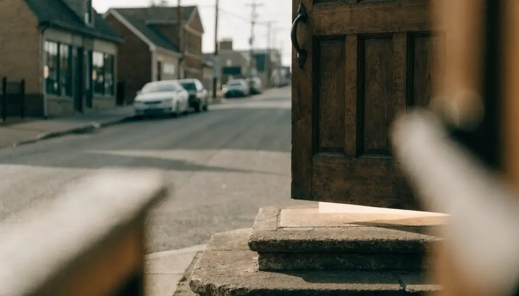 A plain wooden church door standing open with warm light spilling onto stone steps