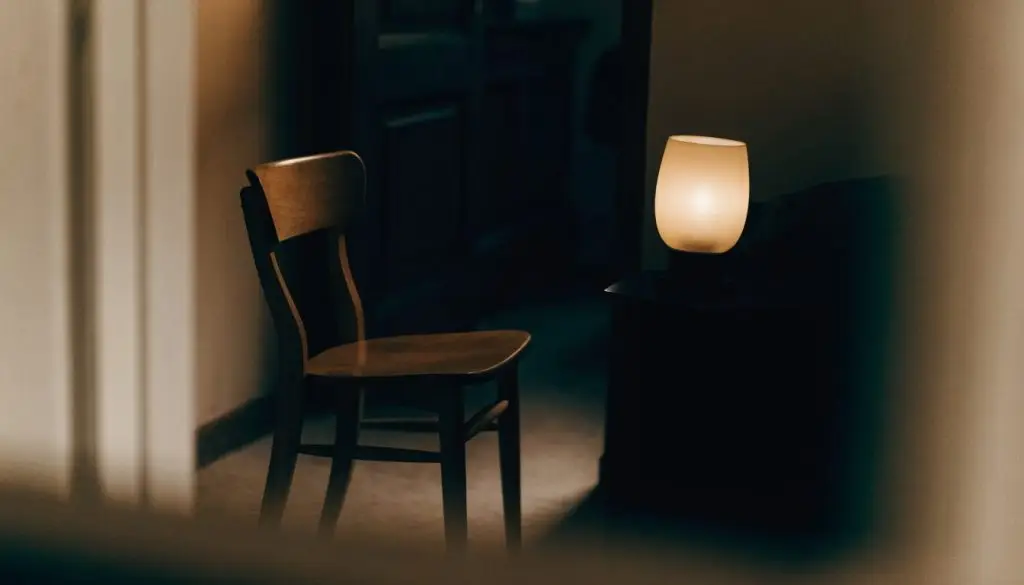 A single lamp lit beside an empty wooden chair in a quiet dark room