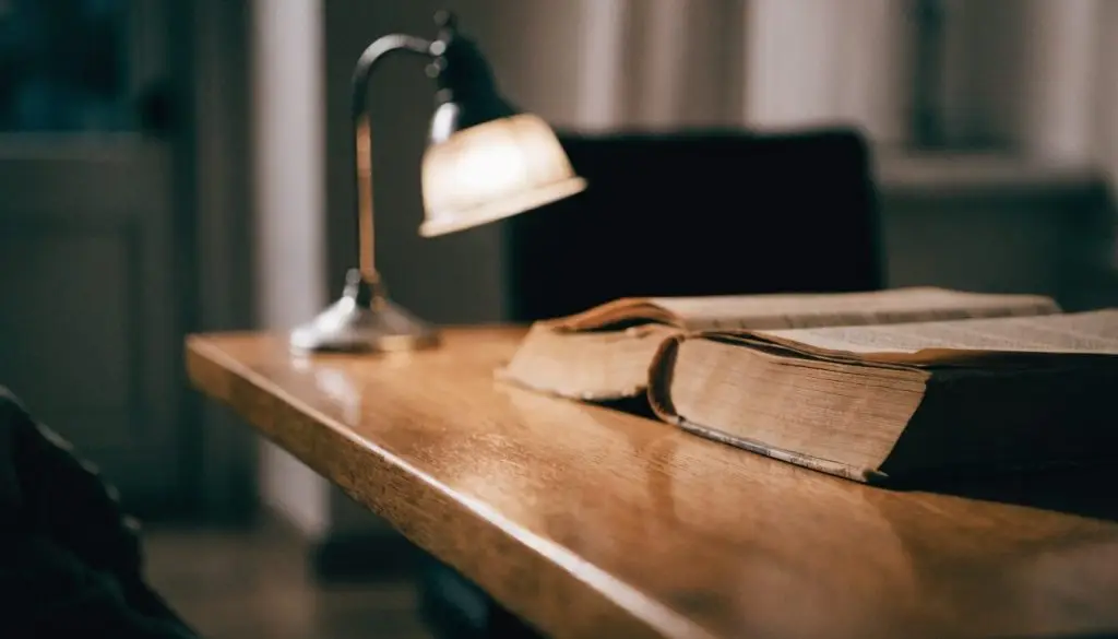 A stack of old cloth-bound books and reading glasses on a wooden table