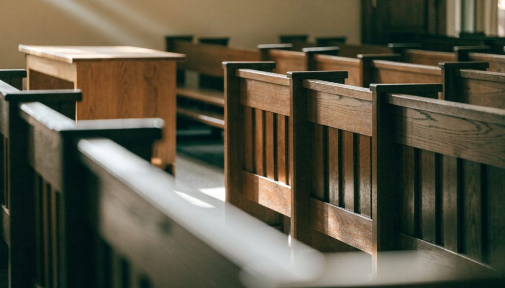 Empty wooden pews lit by soft morning sunlight streaming through tall windows.