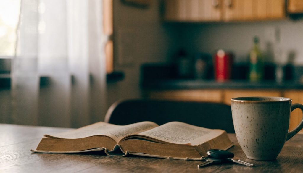 A stack of old books and reading glasses on a wooden desk in warm afternoon light.