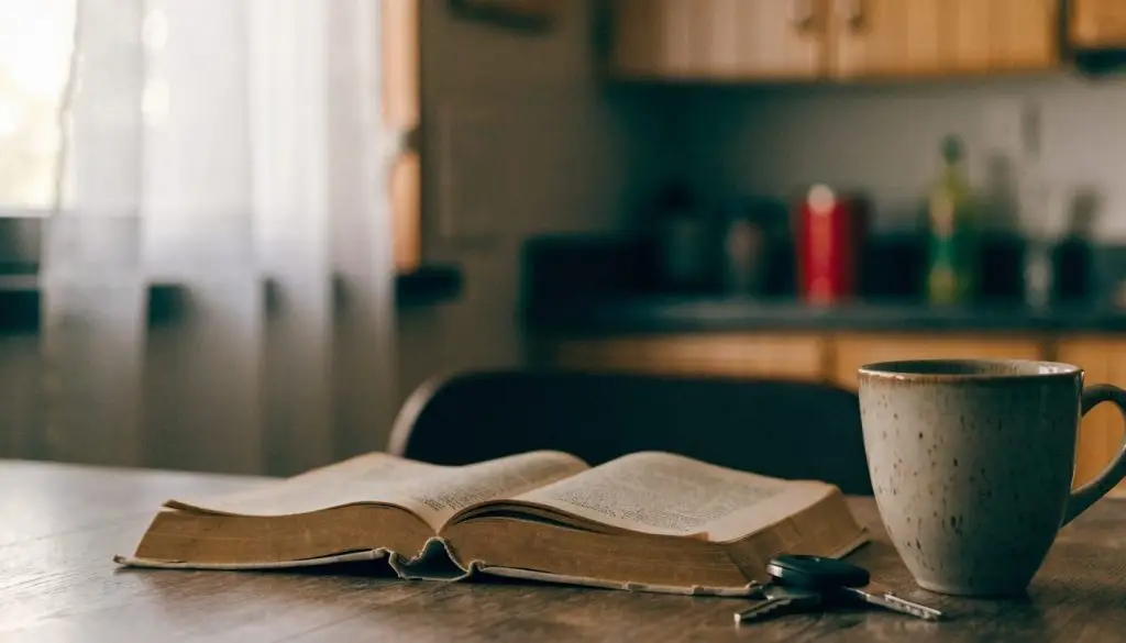 A stack of old books and reading glasses on a wooden desk in warm afternoon light.