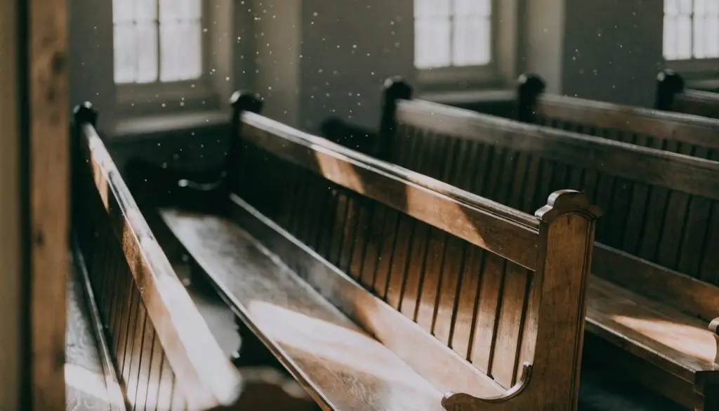 Empty wooden pews lit by soft morning sunlight through tall windows