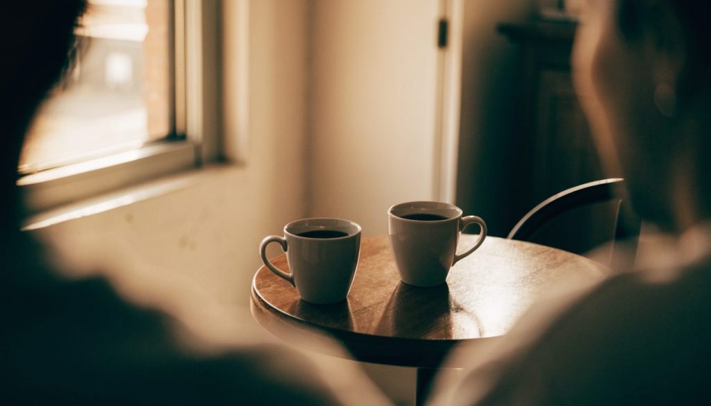 Two plain coffee mugs facing each other on a wooden table in warm afternoon light